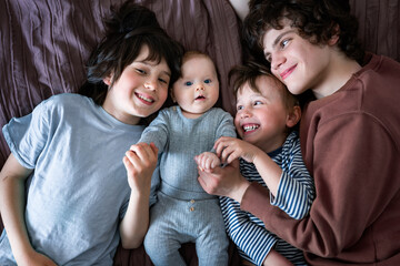 Portrait of three brothers lying on bed with their baby sibling, positive children of different...