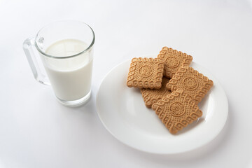 Glass of milk with cookies in plate on white background.