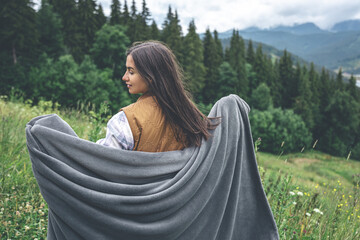 A young woman wrapped in a blanket in the mountains.