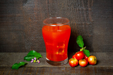 Acerola or Barbados cherry juice in glass and fresh acerola cherry fruits on rustic wooden table.