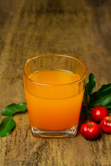Acerola or Barbados cherry juice in glass and fresh acerola cherry fruits on rustic wooden table.