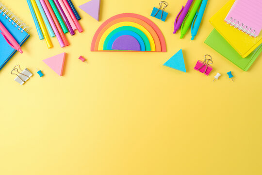 Back to school concept with notebooks, pens and rainbow sticky notes on yellow background. Top view, flat lay