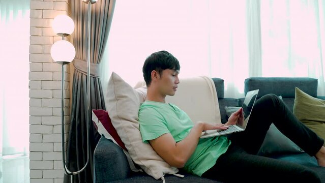 4K, A young man in a green shirt lying on the sofa playing on a laptop computer, His lover's boyfriend brought a ring in a red box, in order to marry him, inside the house, friendship LGBTQ couples.