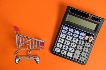 Shopping cart and calculator on orange background, family budget and shopping.