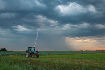 A lightning bolt strikes down from a dramatic stormy sky behind a tractor in the countryside