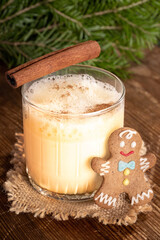Glass with traditional Christmas eggnog and small gingerbread man on rustic wooden table.
