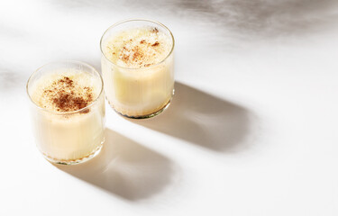 Two glasses with Christmas eggnog with cinnamon on white with beautiful shadows. Selective focus.