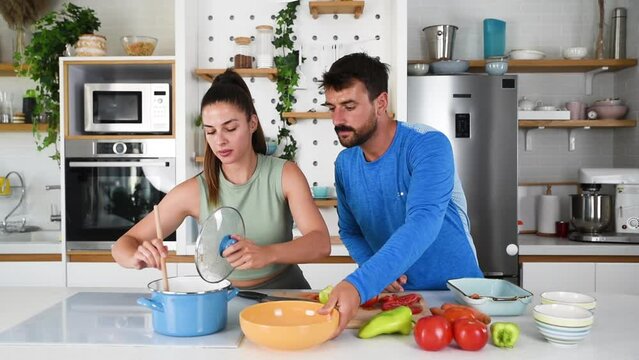 Young sporty man and woman couple cutting and together cooking fresh natural vegetables at kitchen and cooking for healthy lunch. Self care yoga nutritionists having healthy meal after home workout.