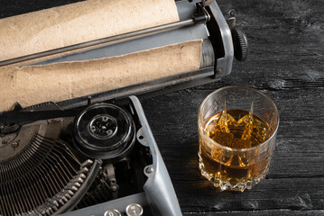 Whiskey in the glass and retro typewriter on the old wooden table background close up.