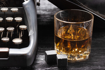 Whiskey in the glass and retro typewriter on the old wooden table background close up.