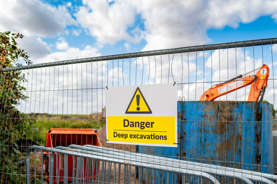 Generic yellow triangle warning sign describing Deep Excavations at a pipeline laying site. Beyond the fence its a 20ft deep hole which poses a hazard to the public.