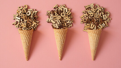 Three cone ice creams formed with a ball of wooden letters on a pink background