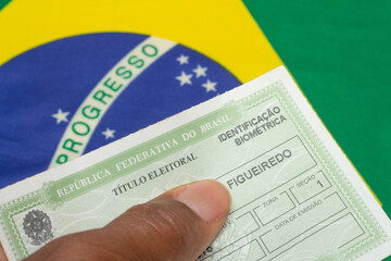 LAURO DE FREITAS, BRAZIL - August 19, 2022 : hand holding brazilian election document  near brazilian flag
