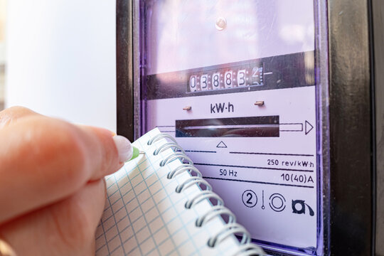 Woman with pen and notepad writes the electricity meter readings at home. Payment of utility services.
