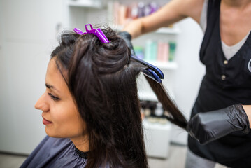 Fototapeta premium Hairdresser using a hair straightened to straighten the hair. Hair stylist working on a woman's hair style at salon.