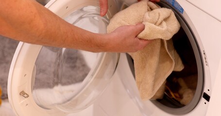 Load washing machine with clothes loaded by man to be cleaned.