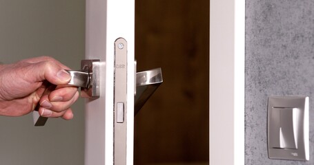 To open the door. Modern white door with chrome metal handle and a man's arm. Elements of interior closeup.