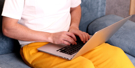 Naklejka premium Close up of a man typing on laptop computer while sitting on a couch.