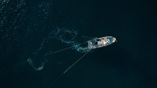 Commercial trawler boat tows netting bags which through water to catch sardines, aerial top view