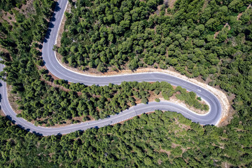 Aerial top view of curves at a highway through thick pine forest as seen on the island of Evia, Greece