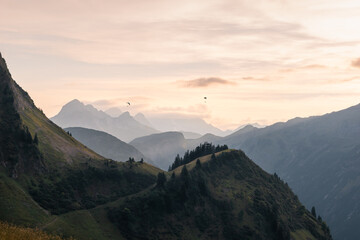 View from the Enzianhütte to the Allgäu mountains at sunset with two paragliding in the air.
