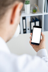 Virtual connection. Digital mockup. Work place. Unrecognizable man holding smartphone with blank screen in hand light office room interior.
