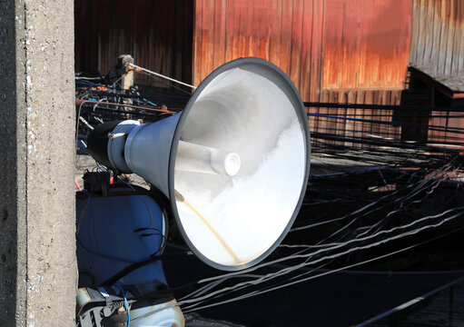 White vintage horn loudspeaker installed on the pole for boardcasting information in community with messy wires in background.