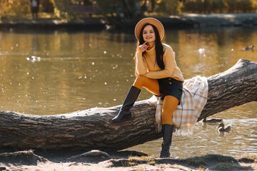 A smiling beautiful young woman in a fashionable hat and casual clothes enjoys a walk alone in an fall park in the autumn outdoors. Selective focus