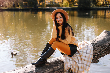 A smiling beautiful young woman in a fashionable hat and casual clothes enjoys a walk alone in an fall park in the autumn outdoors. Selective focus