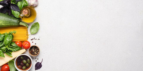 Italian food on white background. Fresh green and red basil, tomatoes, parmesan cheese, olives, olive oil, spices, spaghetti pasta, zucchini. Ingredients for cooking vegan dishes