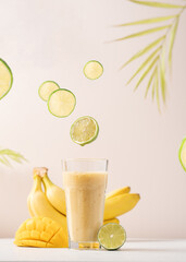 Banana mango smoothie in a tall glass on a light background. Diet breakfast. Tropical fruit drink concept