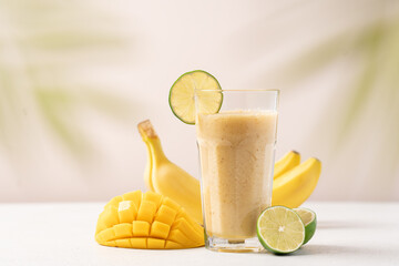 Banana mango smoothie in a tall glass on a light background. Diet breakfast. Tropical fruit drink...