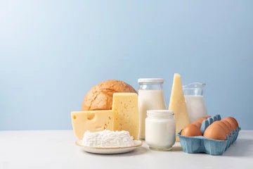 Fotobehang Variety of dairy products on blue background. Jug of milk, cheese, butter, yogurt or sour cream, cottage cheese, bread and eggs. Farm dairy products concept © Anna Puzatykh