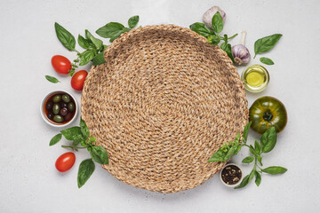 Italian food on white background around wicker round tray. Fresh green and red basil, tomatoes, parmesan cheese, olives, olive oil, spices, spaghetti pasta. Mediterranean Kitchen
