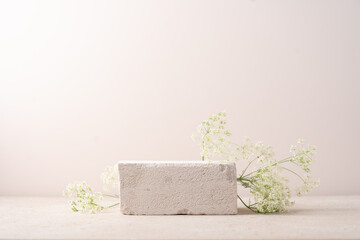 Minimal concrete background for branding and packaging presentation. Textured stone on a beige background with white flowers