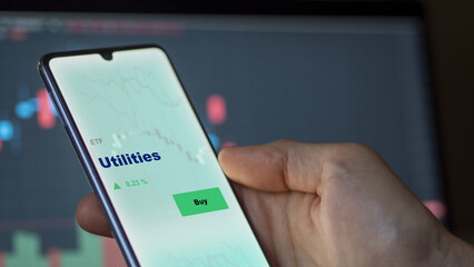 An investor's analizing the utilities etf fund on a screen. A phone shows the prices of utility.
