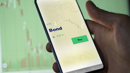 An investor's analyzing the bond etf fund on a screen. A phone shows the prices of bonds.