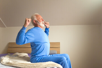Senior man stretching while sitting in bed after waking up in the morning