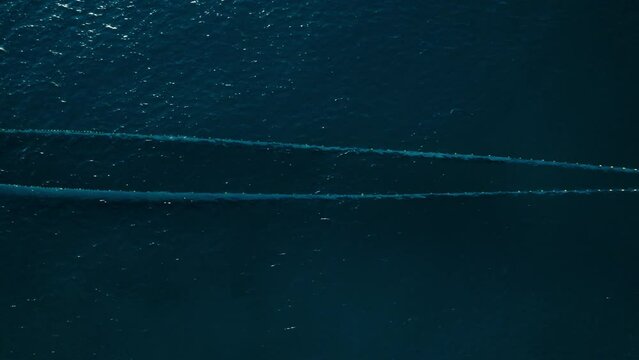 Tracking shot of big trawl with netting bags towed through water to small boat with fishermen working hard to pull out caught fish. Deep blue waters of open sea. Top view aerial shot