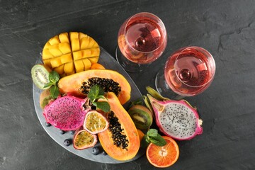 Delicious exotic fruits and wine on black table, flat lay
