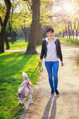 Young woman walking her husky pet dog in the park on sunny spring day