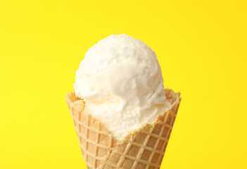 Delicious ice cream in waffle cone on yellow background, closeup
