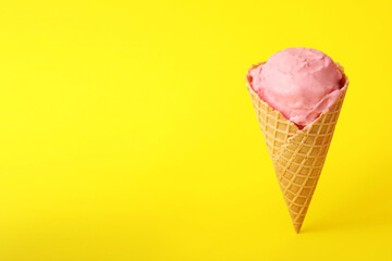 Delicious pink ice cream in waffle cone on yellow background. Space for text