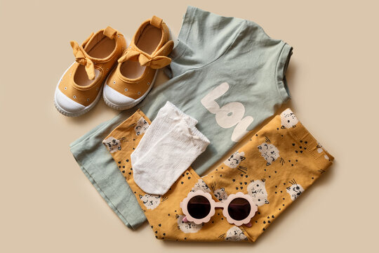 Stylish child clothes, shoes and accessories on beige background, flat lay