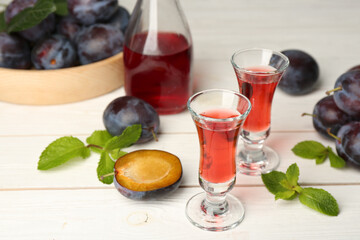 Delicious plum liquor, ripe fruits and mint on white wooden table. Homemade strong alcoholic beverage