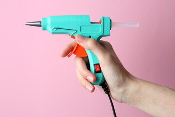 Woman holding turquoise glue gun with stick on pink background, closeup