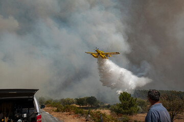 Avião no combate aos incêndios com algumas pessoas na estrada a ajudar os bombeiros e com muito...