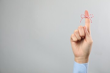Woman showing index finger with tied bow as reminder on light grey background, closeup. Space for text