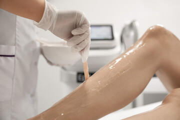 Professional cosmetologist applying gel on client's leg before laser epilation procedure in salon, closeup