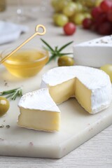 Tasty brie cheese with olives and rosemary on white board